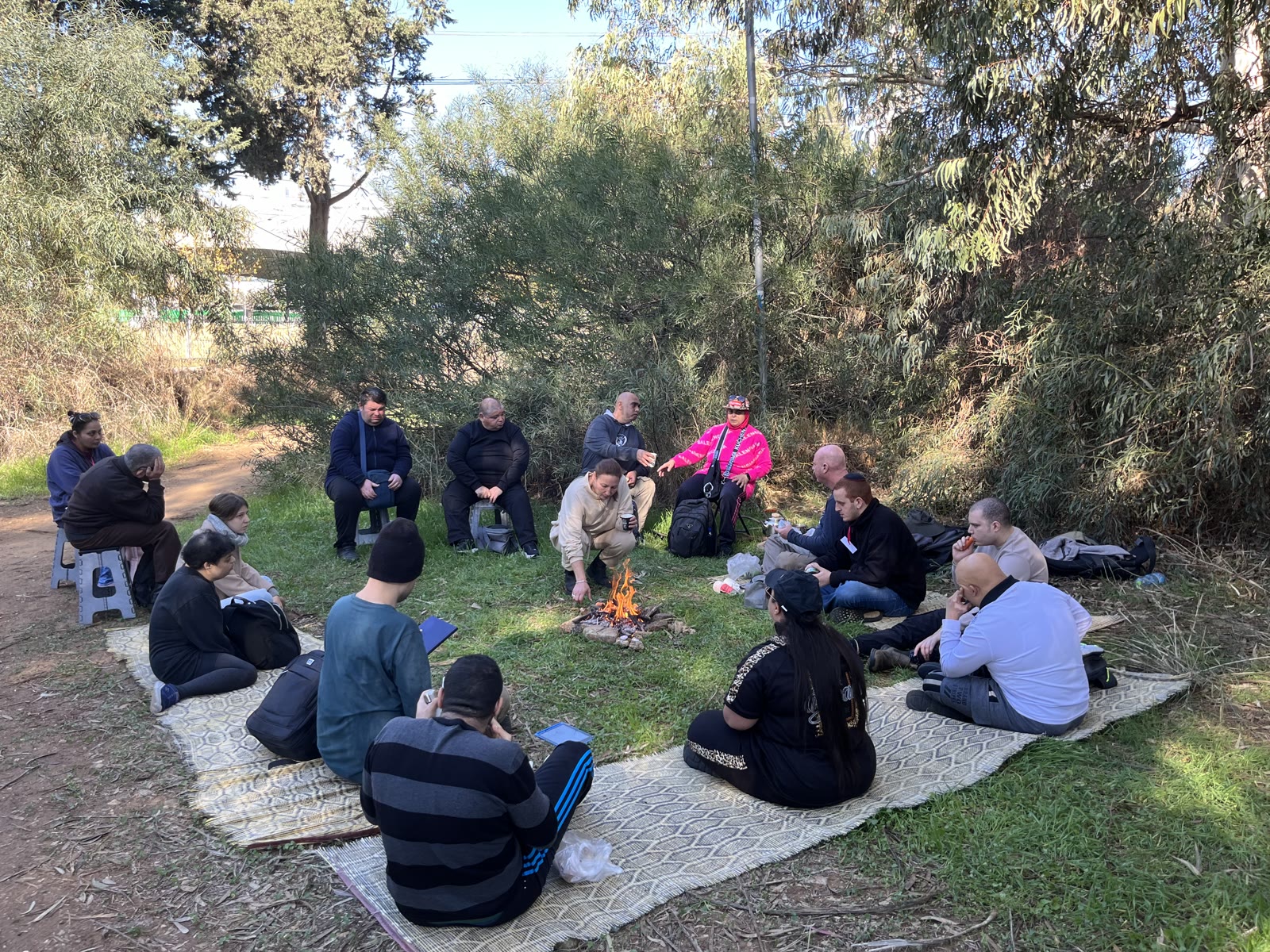חברי הקבוצה יושבים יחד סביב מדורה בטבע